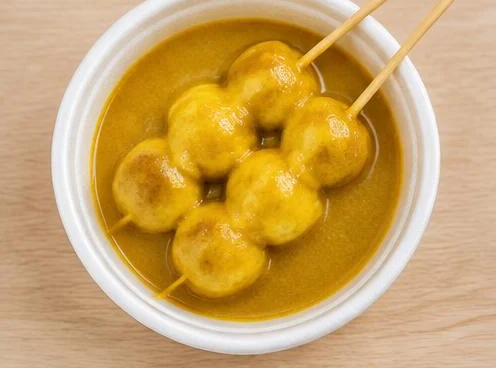 Curry fish balls coated in yellow curry sauce on a wooden board