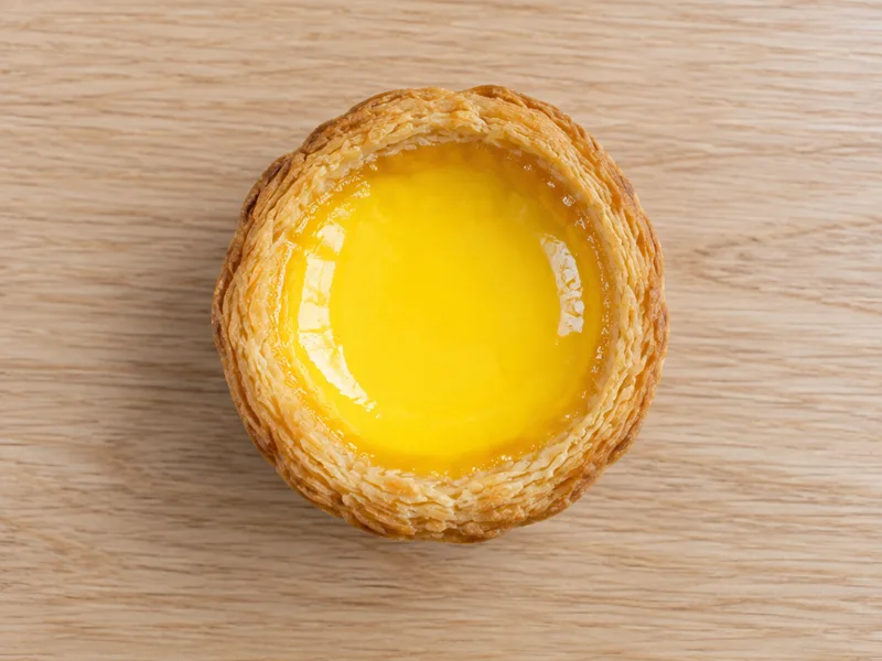 Golden egg tart with flaky pastry and custard on a wooden board