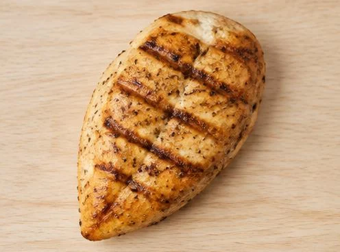 Grilled chicken breast with browned grill marks on a wooden board