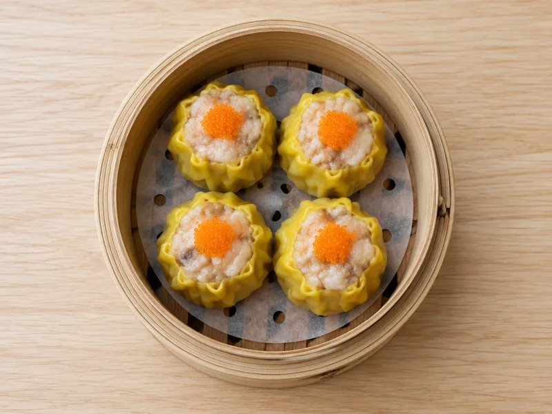 Four siu mai dumplings in a bamboo steamer on a wooden table
